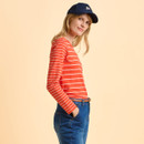 A person in a red striped shirt and blue jeans, wearing a navy cap, smiles subtly against a soft peach background, conveying a casual, relaxed vibe.