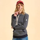 A woman with long hair smiles playfully, wearing a red cap and a navy striped hoodie, holding a strand of hair. She stands against a soft beige background.