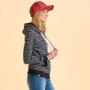 Side view of a person wearing a red cap, striped hoodie, and jeans against a beige background. The pose is relaxed and casual.