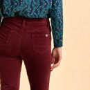 A person in burgundy pants with back pockets and a blue-green leafy patterned shirt stands against a beige background, exuding a casual vibe.