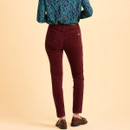 Person in burgundy corduroy pants and brown shoes, with a teal and blue patterned blouse. They stand against a beige background, creating a casual, stylish look.