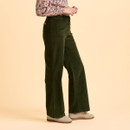 A person wearing a floral blouse, green corduroy wide-leg pants, and beige sneakers stands against a soft peach background, conveying a relaxed and stylish vibe.