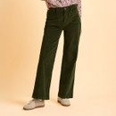 Person wearing green corduroy pants, floral blouse, and beige sneakers on a light beige background. The outfit conveys a casual and stylish vibe.