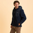 Man in a navy fleece hoodie with hands in pockets, looking to the side. The background is a soft beige, conveying a casual and relaxed tone.