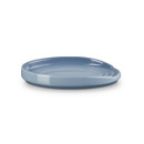 Angled side view of a light blue Le Creuset spoon rest showing shallow curved surface and raised lip.