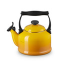Angled front view of a Le Creuset enamel-on-steel whistling kettle in nectar yellow with a black handle and spout lever.