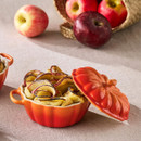 Le Creuset Mini Pumpkin Casserole Dish in Volcanic orange filled with baked apple pastry roses, placed on a neutral fabric background with fresh apples in the background.