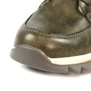 Close-up of a green leather shoe, featuring a rounded toe with a beige sole and dark brown tread. The texture is smooth, conveying a casual tone.
