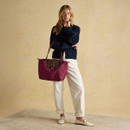 Full-body view of woman holding a berry red tote bag, styled with casual white trousers.