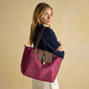 Woman carrying a berry red tote bag over her shoulder with navy knit cardigan.