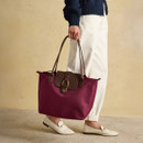 Close-up of woman’s hand holding the berry red tote bag by its brown leather handles.