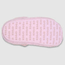 The image shows the pink sole of a slipper against a gray background, featuring a repeated "crocs" logo pattern in light brown, conveying comfort and style.