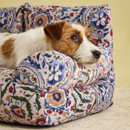 Close-up of Wire Fox Terrier lying on Joules floral sofa-style pet bed with cushioned armrest.