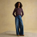 Full length view of a woman wearing a navy striped long sleeve top with mustard and pink stripes, styled with wide leg blue jeans and tan shoes.