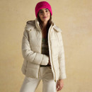 Woman in a pink knitted beanie hat and cream padded jacket smiling, styled for a casual winter look.