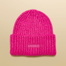 Flat lay of a bright pink knitted beanie hat with a ribbed turn-up cuff and Joules logo patch.