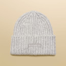 Flat lay of a soft grey knitted beanie hat with ribbed turn-up cuff and Joules logo patch.