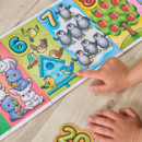 A child’s hands point to a colourful counting book with numbers 6, 7, and 8. The pages feature illustrations of animals and apples.