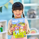 A young girl smiles, holding a colourful "Bluey Grannies Game" box with cartoon characters. The background is bright and cheerful, enhancing the playful tone.