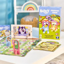 "Bluey Grannies Game with vibrant board, cards, and character pieces on a table. The box depicts cartoon characters joyfully dancing. Playful, fun atmosphere."