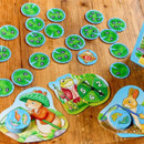 Card game on a wooden table featuring colourful animal illustrations, lily pad tokens, and a spinning wheel. The vibe is playful and engaging.