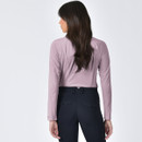 A woman with long brown hair stands facing away, wearing a light pink long-sleeve top and black trousers. The background is plain white, conveying a calm tone.