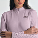 A woman wearing a light purple Weatherbeeta top with a high collar and long sleeves, logo on chest and sleeve. She stands with arms crossed, exuding confidence.