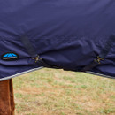 Close-up of a navy blue Weatherbeeta horse blanket with straps, partially covering a brown horse. Set against a grassy background, conveys practicality.