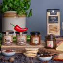 Edinburgh Preserves Farmhouse Pâtés and chutneys with sesame biscuits, fresh herbs, spices, and cheese on a rustic wooden table.