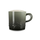 A green ceramic mug with embossed holly leaves and a cream interior, viewed from the side.