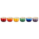 Six Le Creuset mini ramekins in red, orange, yellow, green, blue, and purple, lined up in a row against a white background. Six Le Creuset mini ramekins in red, orange, yellow, green, blue, and purple, lined up in a row against a white background.