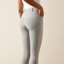 A person wearing light gray, form-fitting riding breeches with subtle dotted texture, paired with a white top. The tone is stylish and sleek.