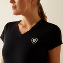 Woman in a black V-neck t-shirt with an emblem on the chest, facing left. The background is neutral, and the atmosphere is calm and focused.