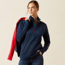 Woman in a navy pullover with a red jacket draped over her shoulder. She looks to the side, conveying a confident and thoughtful expression.