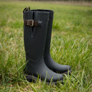 A pair of sleek navy rubber boots with buckles stands in a lush grassy field. The scene conveys a sense of readiness for outdoor adventures.