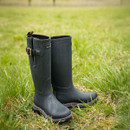 Dark navy rubber boots stand on lush, wet grass. A metal buckle adds detail, while water droplets suggest a fresh rain. Outdoorsy and practical vibe.