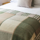 A green, cream and beige checked wool blanket laid across the end of a neatly made bed.