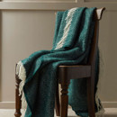 A teal wool blanket with a herringbone pattern draped over a wooden chair.