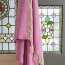 A pink wool blanket with a beehive pattern and cream fringe draped in front of stained glass windows.