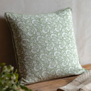A square cushion with a sage green and white floral pattern placed on a wooden surface.
