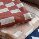 A nutmeg throw with a geometric block pattern stacked with other folded throws.
