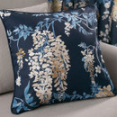 A navy blue cushion with a floral design featuring cascading beige and light blue wisteria flowers and leaves, placed on a grey sofa.