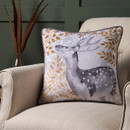 A square cushion on a beige armchair, featuring a grey watercolour-style deer surrounded by golden leaves and branches.