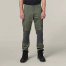 A man wearing green cargo trousers with darker knee patches and black hiking boots, standing against a plain grey background. Casual and outdoorsy style.