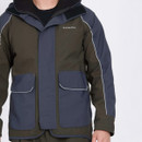 The person wearing a two-toned jacket with gray and olive green colours, featuring large front pockets and white piping, conveying a casual outdoor vibe.