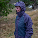 Person in a hooded rain jacket smiles while standing in a grassy area. Raindrops are visible on the jacket, creating a joyful and serene mood.