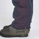 Close-up of two legs wearing dark blue and burgundy pants, tucked into rugged, mud-stained boots on a plain white background.