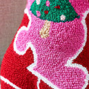 Close-up of the textured boot-shaped cushion, highlighting the embroidered Christmas tree detail against a pink background.