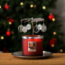Red Christmas candle with silver carousel topper decorated with hanging bauble ornaments, glowing warmly in front of a blurred Christmas tree with gold star-shaped lights.