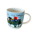 White mug with a light blue background, featuring an illustration of a woman in a red bobble hat sitting on a green bench with three dogs in the snow. Above them is the phrase “Crazy Dog Lady” in playful script. The inside rim is decorated with blue polka dots.
